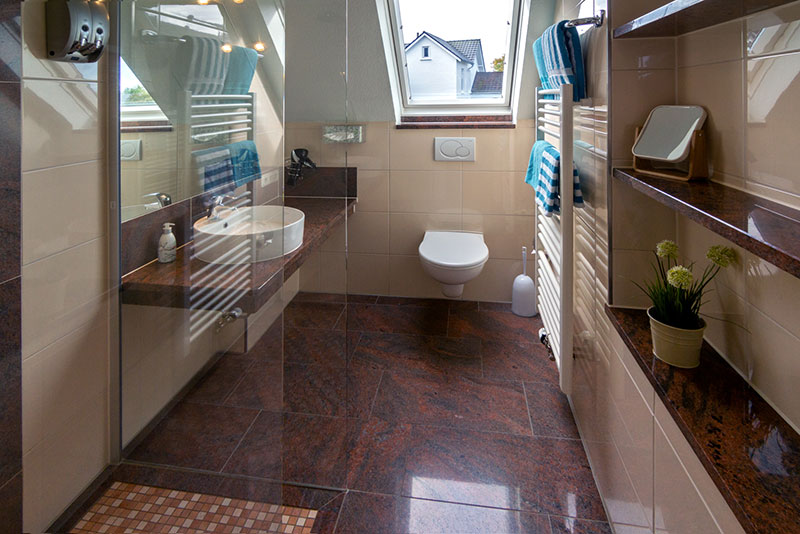 badezimmer mit Dachfensterausblick, links Dusche , Waschbecken, mittig das WC-Becken und rechts Handtuchhalter mit frischen blau-weißen Handtüchern