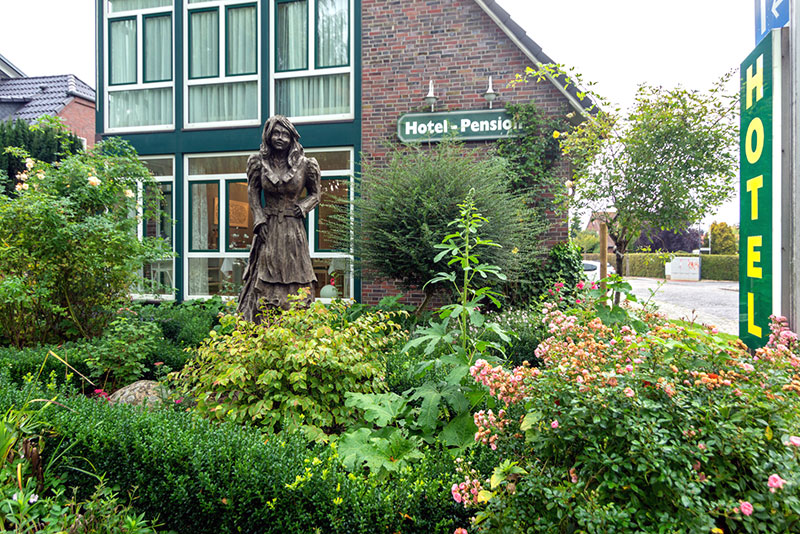 Blick auf Außenansicht und Teil des Vorgartens des Hotels am Elisabethufer mit hölzerner Frl. Maria Statue